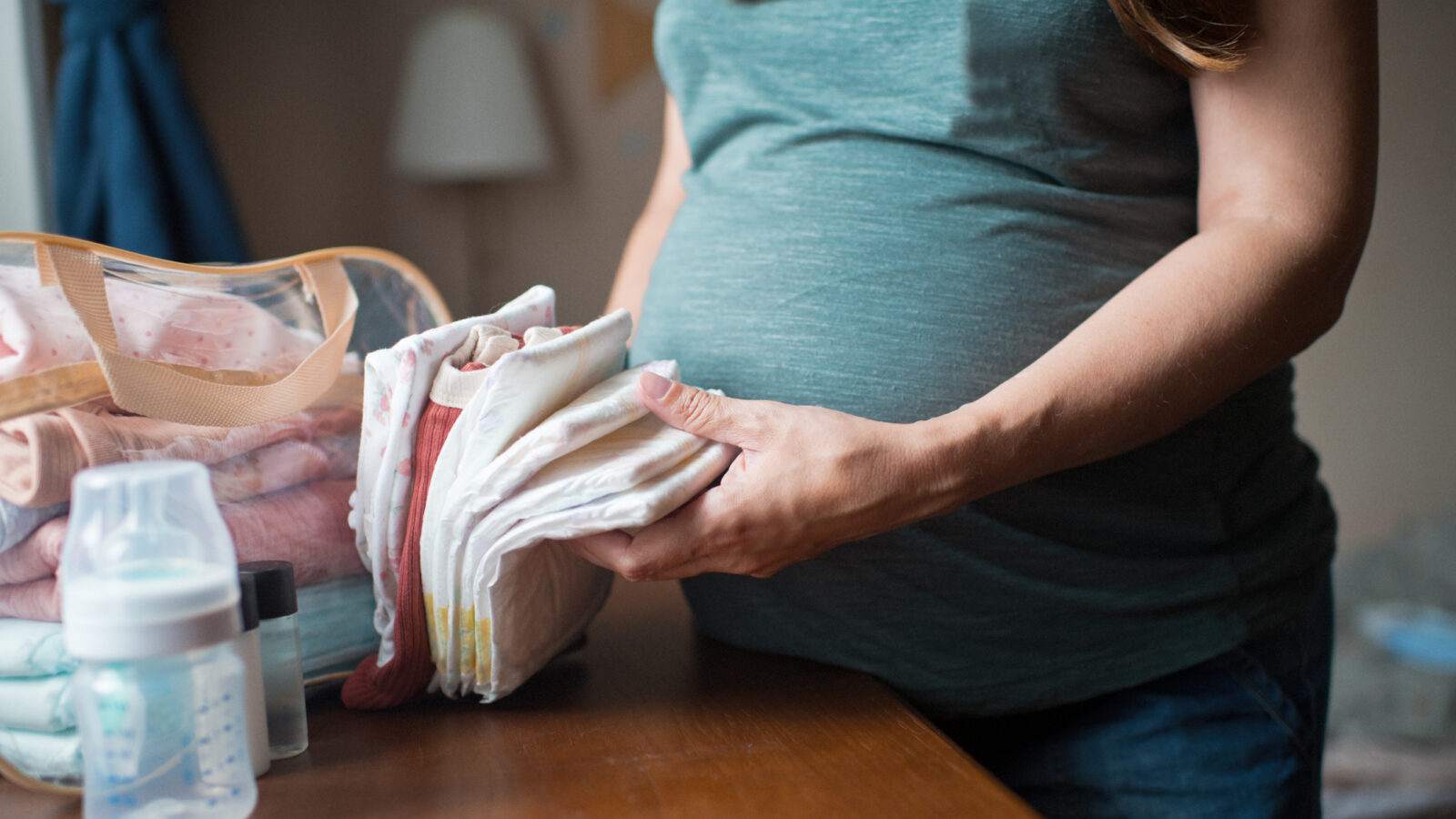 Pregnant woman at home preparing bag for newborn baby